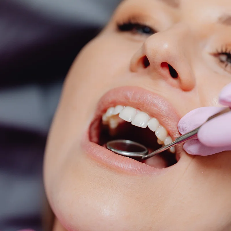 Close-up of dentist using mirror tool to examine female patient's teeth before oral surgery