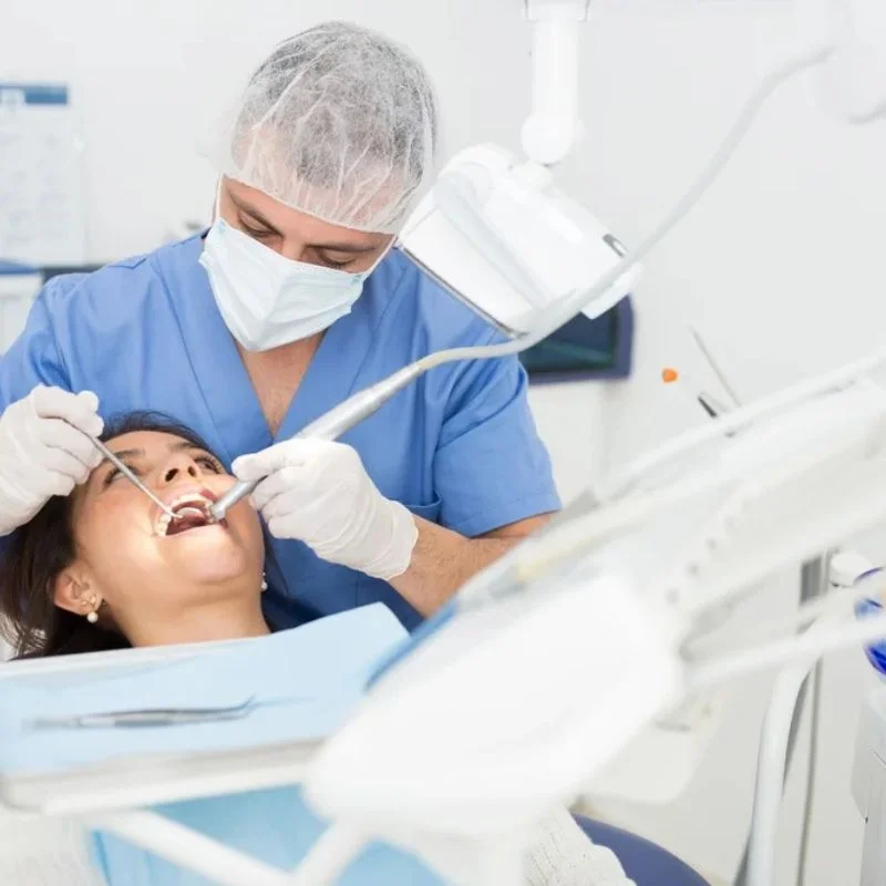 Dentist performing tooth extraction procedure on female patient under dental light