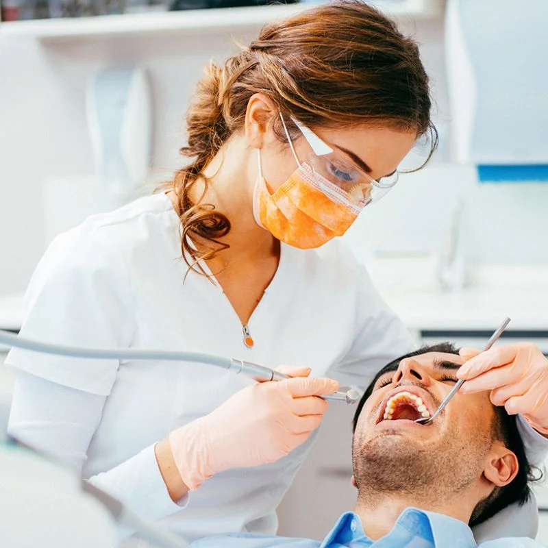 Dentist performing dental restoration procedure on male patient using drill and mirror tools