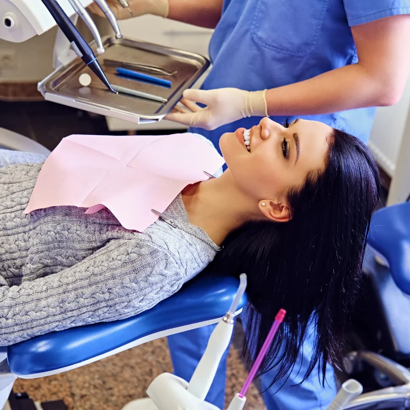 Female patient relaxed in dental chair as dentist prepares dental restoration instruments