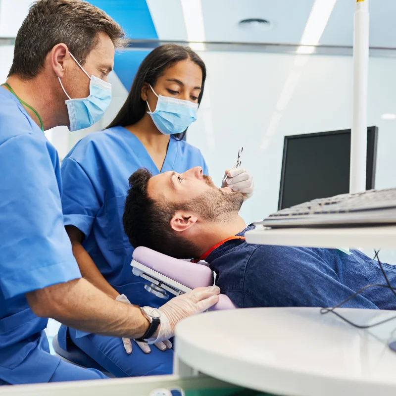 Dentist and dental assistant performing oral surgery procedure on male patient in treatment room