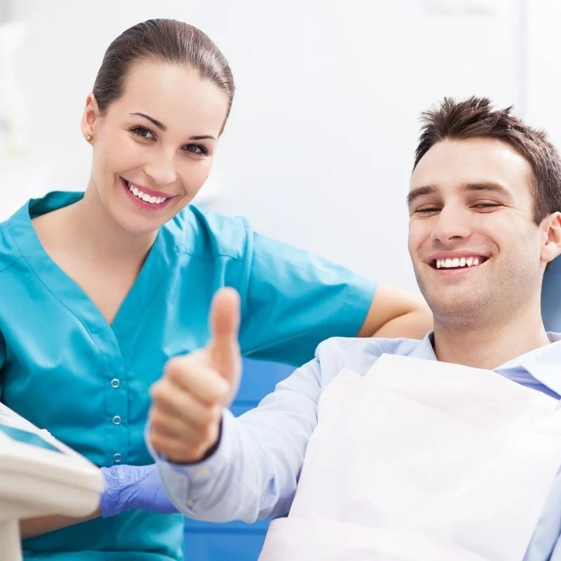 Male patient giving thumbs up in dental chair with dentist smiling after successful tooth extraction
