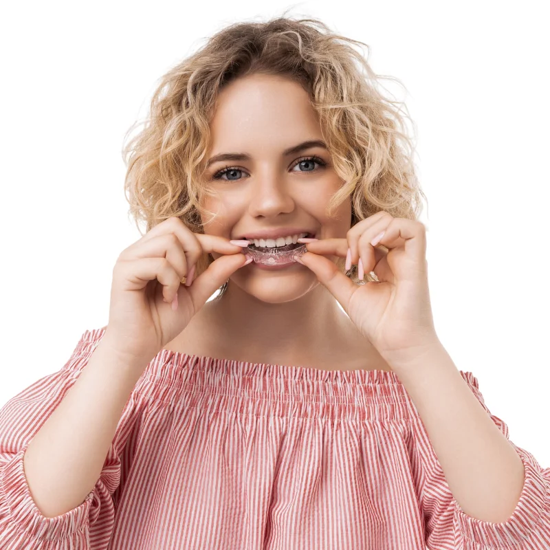 Young woman smiling while holding a removable Invisalign clear aligner