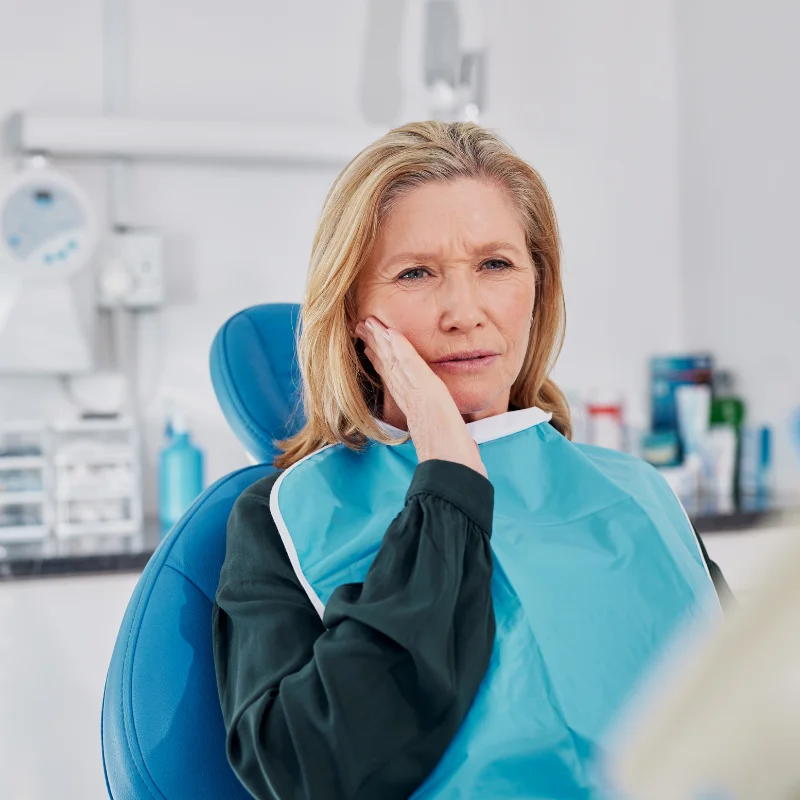 Female patient holding jaw in pain while sitting in dental chair during emergency dental visit
