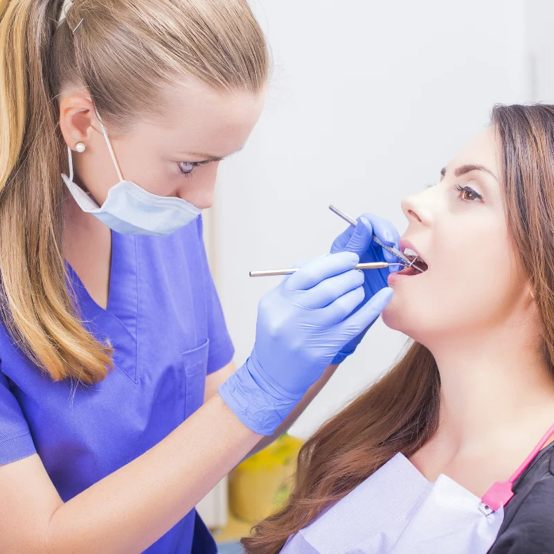 Dentist examining female patient's teeth with mirror and explorer during general dentistry checkup