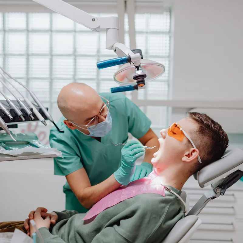Dentist examining teenage patient's teeth under dental light during oral surgery consultation