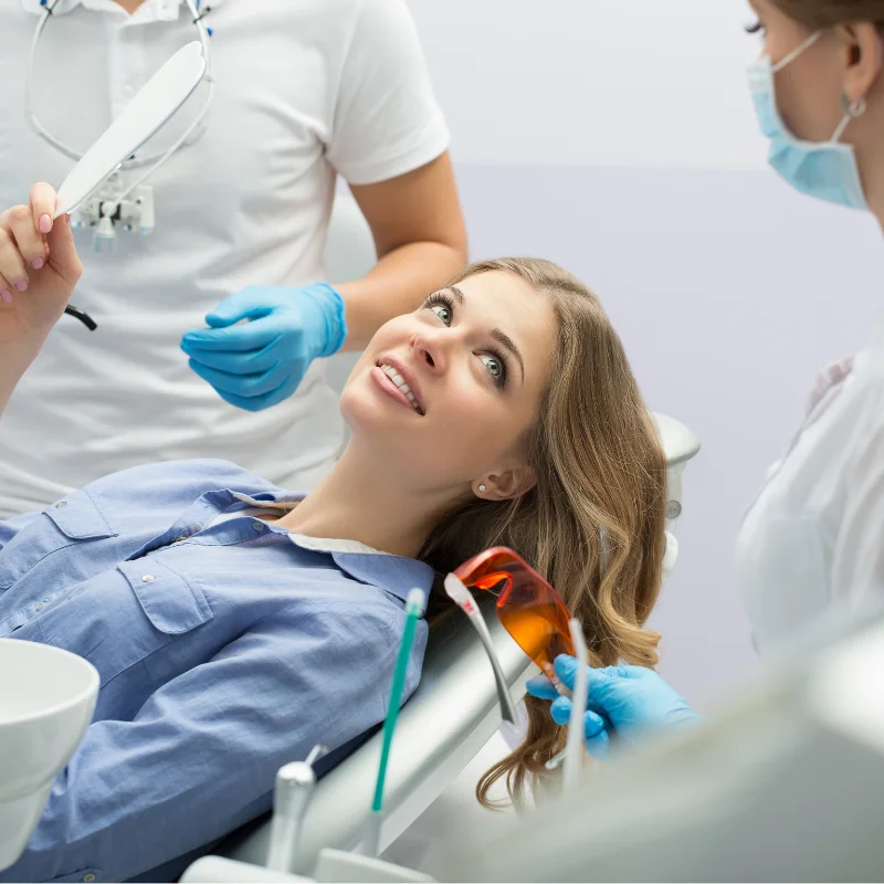 Female patient smiling comfortably in dental chair during general dentistry appointment with two dental staff