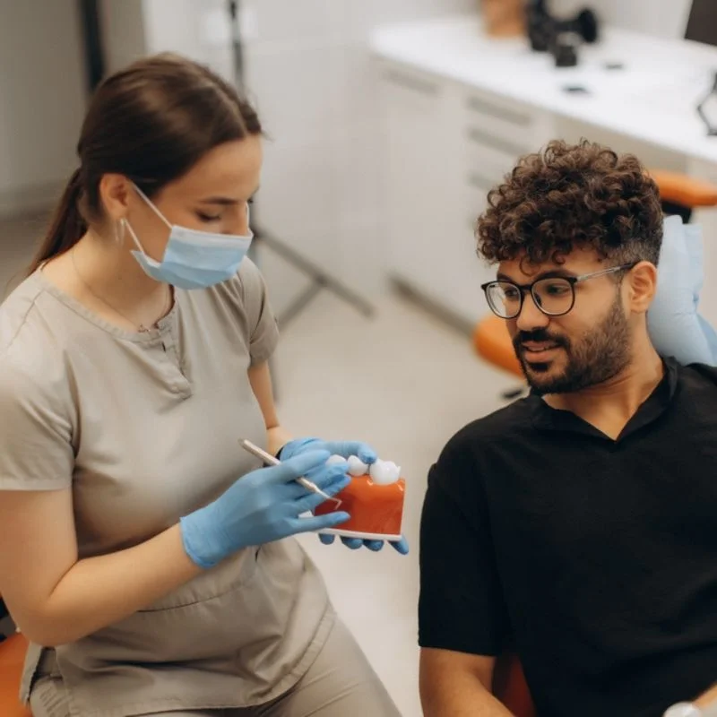 Dentist holding dental jaw model while explaining dental bridge options to male patient