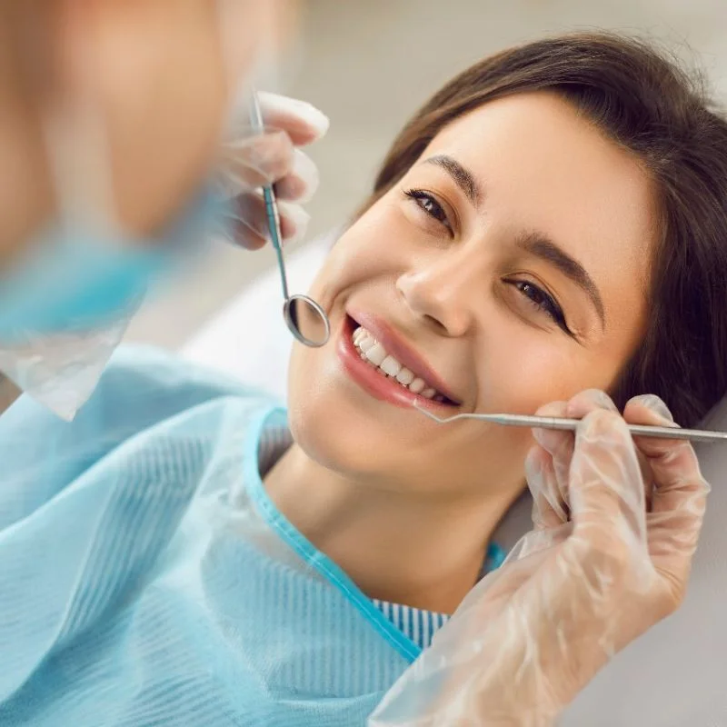 Female patient smiling during routine general dentistry exam with dentist using mirror tool